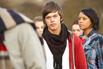 Photo of a teenage Caucasian boy looking serious with other teenagers in the background